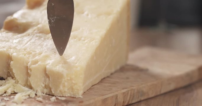 Slow motion slide of female hand cutting hard parmesan cheese