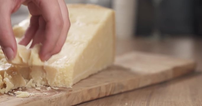 Slow motion slide of female hand taking pieces of hard parmesan cheese from olive board