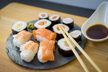 Sushi on a wooden table on black slate plate with soy sauce and chopsticks