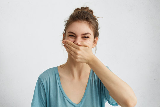 Positive female laughing while having good mood during spare time trying to control her emotions covering mouth with hand. Cheerful woman having fun bursting into laughing keeping hand on mouth