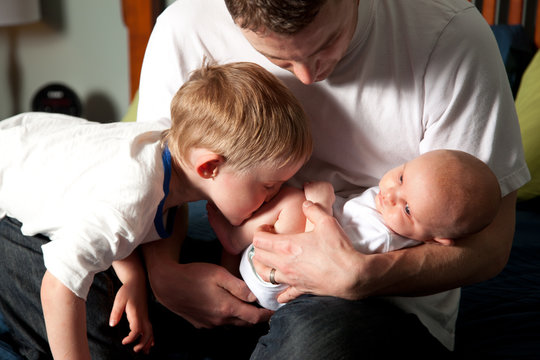 Brother Kisses New Baby, Held By Dad