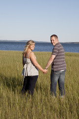 young couple walk on beach grass look back