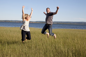 young couple jumps for joy by a beach in summer 