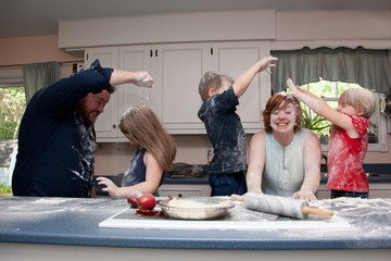 Family with three children having food fight in kitchen.
