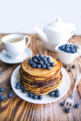 Pancakes healthy breakfast with blueberries, bog whortleberry, cup of green tea, cup of blueberries and teapot on brown wooden background 