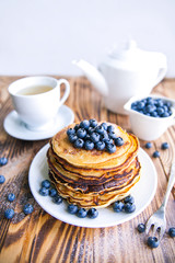 Pancakes healthy breakfast with blueberries, bog whortleberry, cup of green tea, cup of blueberries and teapot on brown wooden background 