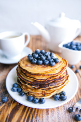 Pancakes healthy breakfast with blueberries, bog whortleberry, cup of green tea, cup of blueberries and teapot on brown wooden background 