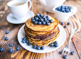 Pancakes healthy breakfast with blueberries, bog whortleberry, cup of green tea, cup of blueberries and teapot on brown wooden background 