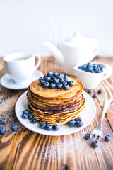 Pancakes healthy breakfast with blueberries, bog whortleberry, cup of green tea, cup of blueberries and teapot on brown wooden background 