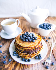 Pancakes healthy breakfast with blueberries, bog whortleberry, cup of green tea, cup of blueberries and teapot on brown wooden background 