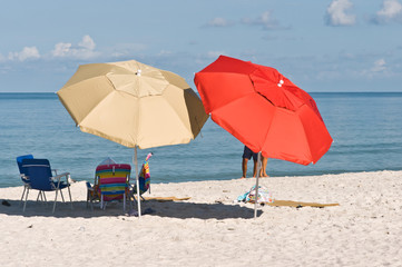 People setting up colorful beach umbrellas and beach chairs on sunny, tropical sandy, beach on the Gulf of Mexico
