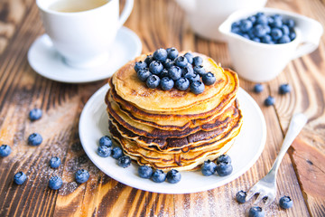 Pancakes healthy breakfast with blueberries, bog whortleberry, cup of green tea, cup of blueberries and teapot on brown wooden background 
