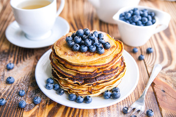 Pancakes healthy breakfast with blueberries, bog whortleberry, cup of green tea, cup of blueberries and teapot on brown wooden background 