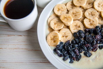 Fitness diet healthy Breakfast which included oatmeal oat porridge with milk, banana and  raisins without sugar and fat with cup of coffee with milk on the white wooden background 