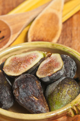Haved and whole organic, local, raw and fresh figs in a artisan ceramic bowl with wood slotted and regular soons on a wood cutting board