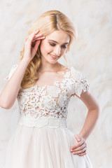 Fototapeta na wymiar fashionable wedding dress, beautiful blonde model, bride hairstyle and makeup concept - cute smiling young woman in white gown indoors on light background, romantic female posing in the studio