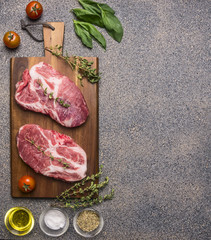 Ingredients for cooking Two fresh raw pork steaks with seasonings and herbs, cherry tomatoes and butter, lined on a cutting board top view border