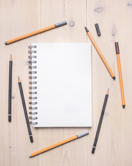 concept of desktop for drawing sketches , notebook with white sheets spread around colored pencils and pens, space for text, border, on a white wooden table