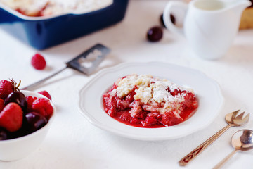 Delicious and juicy berry dessert, pie, coconut Crumble with strawberries, cherry, raspberries, black coffee and milk on a light background