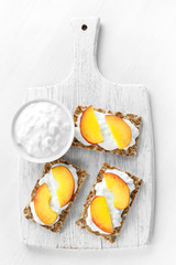 Homemade Crispbread toast with Cottage Cheese and nectarine on white wooden board.