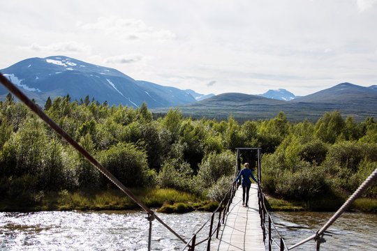 Young woman entering national park via bridge over river, Rondane, Norway