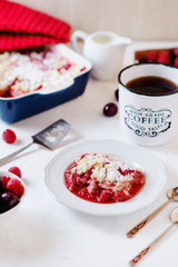 Delicious and juicy berry dessert, pie, coconut Crumble with strawberries, cherry, raspberries, black coffee and milk on a light background