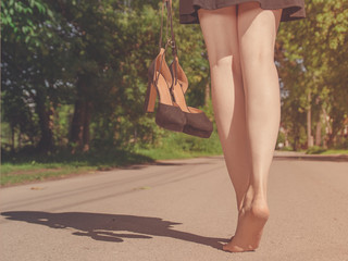 Young pretty woman walking barefoot with heeled shoes in a hand. Summer concept