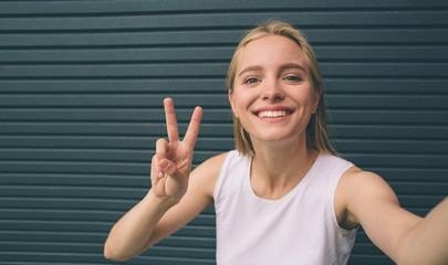 Beautiful young woman making self-portrait on a smartphone on a wall background