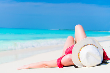 Fototapeta na wymiar Young beautiful girl in hat lying on the beach at shallow tropical water