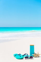 Beach accessories needed for sun protection. Suncream bottles, goggles, flip flops, starfish on white sand beach background ocean