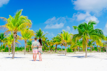 Young couple on white beach outdoors. Happy family enjoy their honeymoon in palm grove