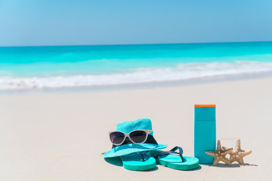 Beach accessories for sun protection. Suncream bottles, hat, sunglasses, flip flops on white sand beach
