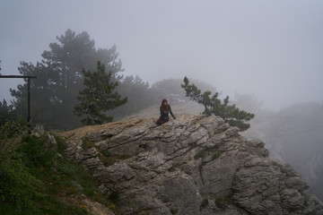 Beautiful young woman sitting on a hillside in the fog