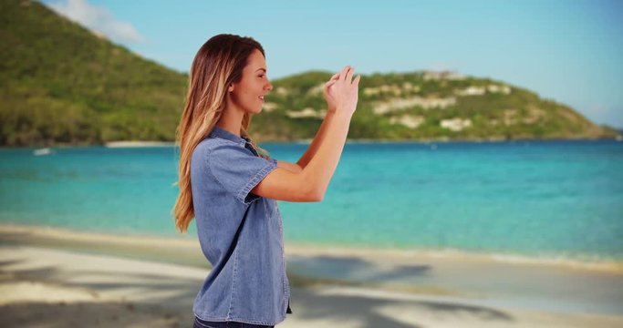 Profile of attractive millennial girl taking a picture with cellphone on the beach. Profile of young Caucasian woman photographing the ocean view while on vacation in summer. 4k 
