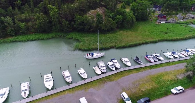 Sailboat leaving a harbor, Cinema 4k aerial view following around a sailboat, exiting a harbor bay, on a summer day, in the finnish archipelago of Turku, Finland