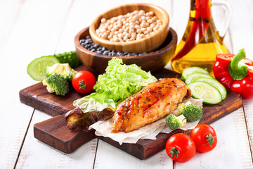 The baked chicken fillet and vegetables. Healthy and fitness food. Meat, salad, vegetables, nuts, beans on a light wooden background. Selective focus. Copy space