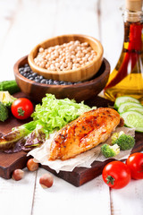 The baked chicken fillet and vegetables. Healthy and fitness food. Meat, salad, vegetables, nuts, beans on a light wooden background. Selective focus. Copy space