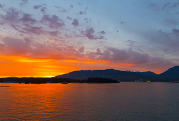 Spectacular sunset in city of Vancouver, BC, Canada. Mountains on horizon during sunset over the sea.