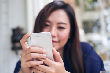 Beautiful Asian woman with smiley face using and looking at smart phone in modern cafe