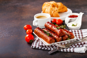 Meat sausages, croissant, coffee and sauces against a dark background. Selective focus.