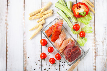 Products for a diet - raw meat of beef and chicken, a salmon and vegetables on a light wooden background. Selective focus.