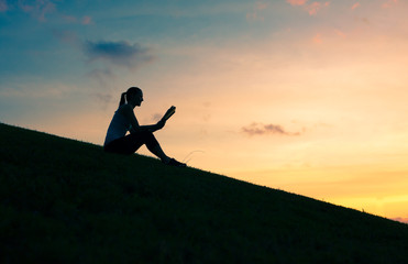 Silhouette of young woman reading a book in the park. 
