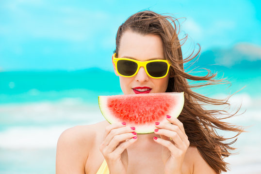 Portrait of beautiful girl on the beach holding slice of watermelon with red painted nails. 