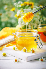 Tasty and healthy honey on white wooden table with flowers of chamomile.