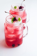 Two glass mugs with red drink, berries and ice close-up on a white background. © ytochka89