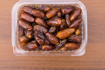 Dried date fruits in plastic container on wooden table. Top view