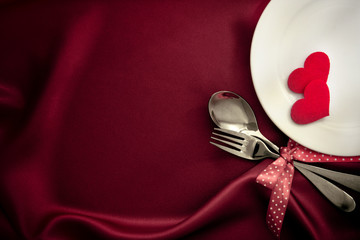 red heart shape with White empty plate with fork and spoon on red silk fabric for love dinner concept
