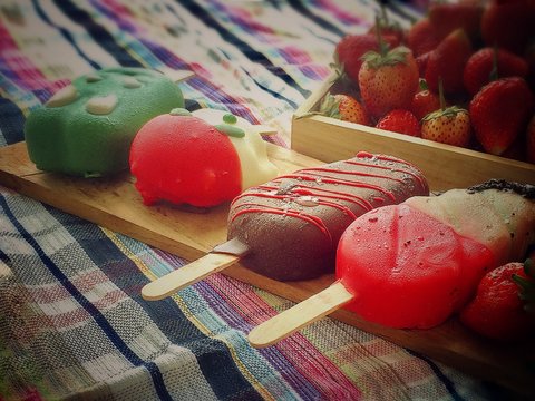 the colorful ice pop put on wood tray beside blurred wood box of strawberry,in vintage design,blurry light around,pastel soft color tone.
