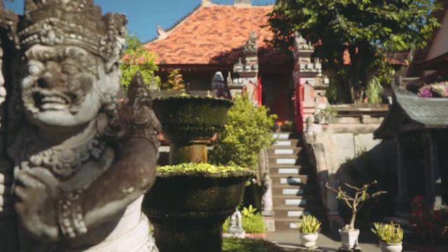 Balinese man stone statue in front of balinese gates and fountain, slide