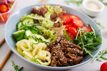 Salad with beef teriyaki and fresh vegetables - tomatoes, cucumbers, paprika, arugula and lettuce in bowl.